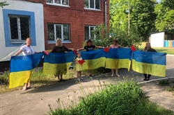[ai] A group of six individuals holding Ukrainian flags with red and yellow hearts attached, standing in front of a building surrounded by greenery. The scene depicts community support and patriotism.